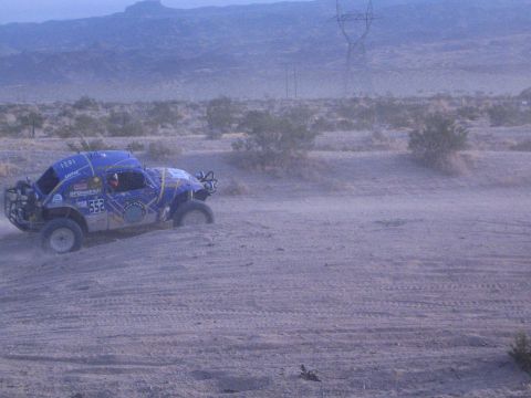 Blue off-road racing Baja Bug number 553 on desert track near power transmission tower