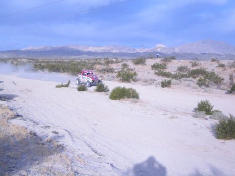 Red white and blue off-road buggy raising dust on sandy desert trail with mountains
