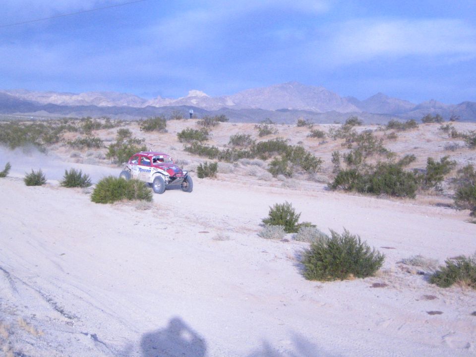 Red white and blue off-road racer cresting sandy desert berm with distant mountains