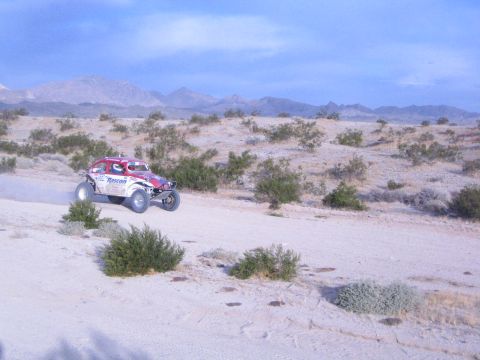Red and white Roscon-marked off-road racer airborne over sandy desert trail