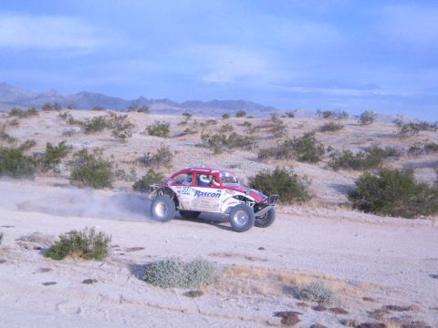 Red white and black Roscon off-road racing car on desert track raising dust