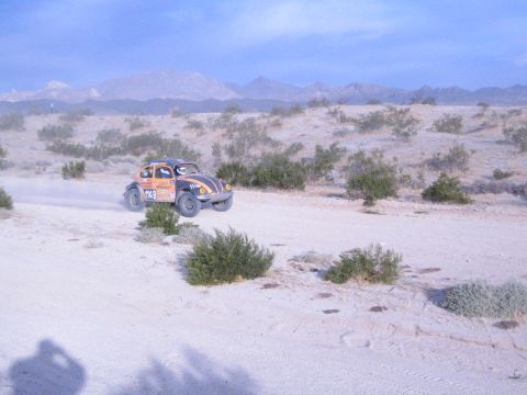 Orange and black off-road racing Beetle catching air over desert trail with mountains