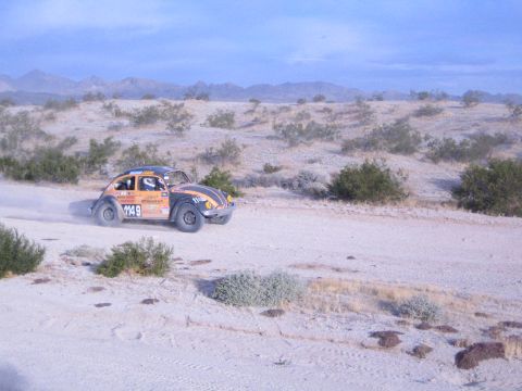 Orange and black off-road racing Beetle number 1148 raising dust on desert trail