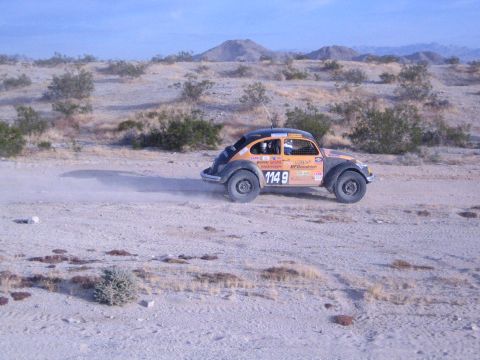 Orange off-road racing Beetle number 1148 in profile raising dust in desert