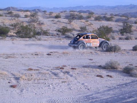 Orange and black off-road racing Beetle number 1149 cornering on sandy desert trail