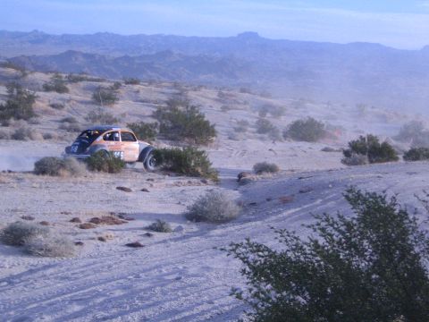 Orange off-road racing Beetle on rocky desert grade with mountain range in haze