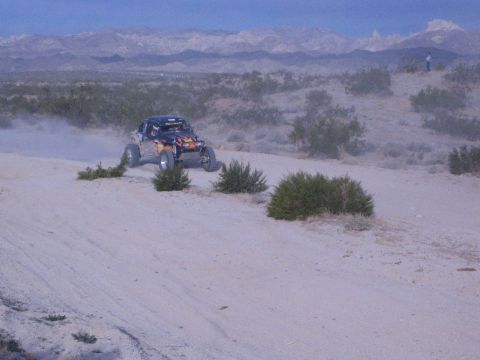 Dark off-road buggy cresting sandy desert dune with snow-dusted mountains behind