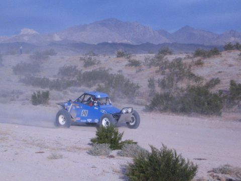 Blue open-cockpit off-road racing car number 949 on desert track with mountains