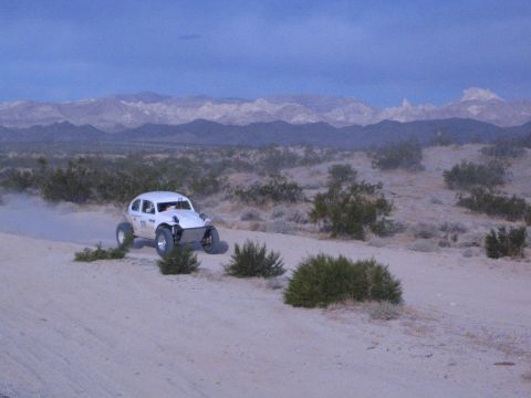 White off-road racing car on sandy desert trail below long snow-capped mountain range