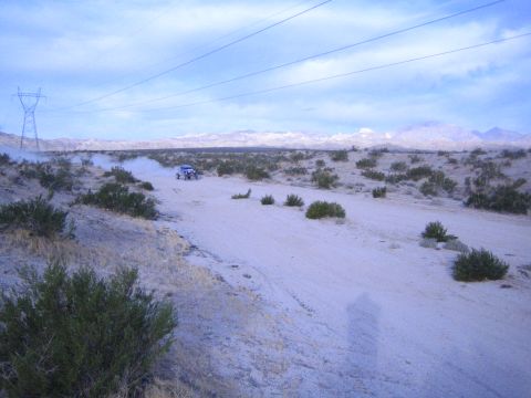 Blue off-road car in distance on sandy desert track under power lines and cloudy sky