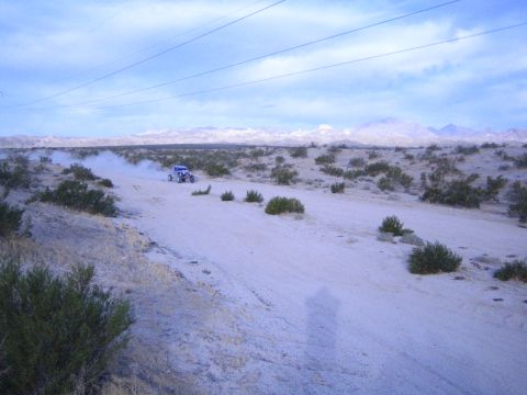 Blue and white off-road car raising dust on desert track under cloudy sky and mountains