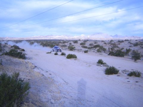 Blue off-road race buggy speeding on a dirt trail through open desert at dusk