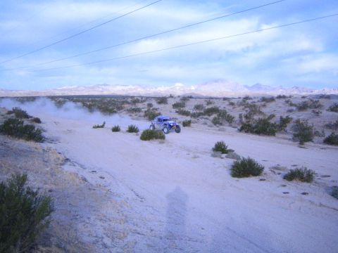 Blue desert race buggy raising dust on a sandy trail with mountains behind