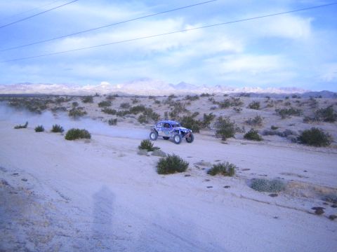 Blue off-road buggy on a desert dirt road beneath power lines and clouds