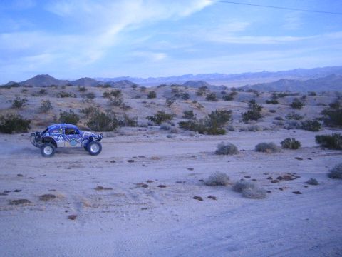 Blue off-road race buggy crossing open desert with mountain range behind