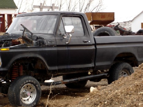 1979 Ford Bronco - This black Ford pickup truck appears to be a 1979 model, with its hood removed and a spare tire in the bed.