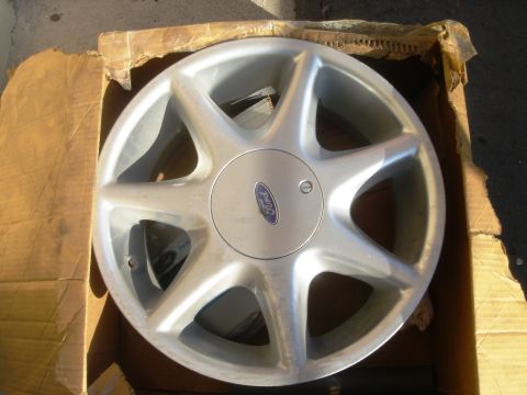 1991 Ford Taurus - This silver wheel features a classic seven-spoke design with a central blue Ford logo.