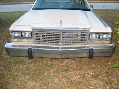 1985 Ford LTD Crown Victoria - The front grille and headlights of a beige Ford sedan are visible, parked on grass.
