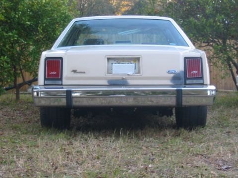 1985 Ford LTD Crown Victoria - Rear view of a cream 1985 Ford Crown Victoria LTD parked on grass with trees in the background.