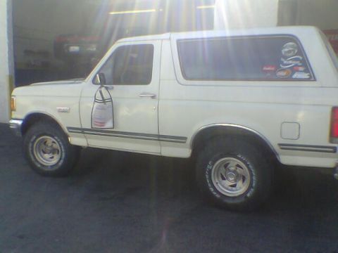 1988 Ford Bronco - A white SUV is parked in front of a garage, with another vehicle visible inside.
