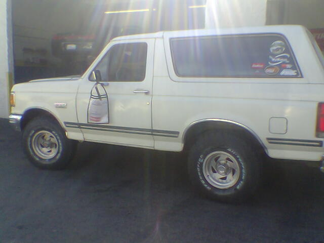 White two-door Ford Bronco side view with alloy wheels and rear-window decals