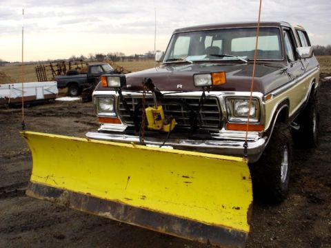 1979 Ford Bronco - A 1978 Ford Bronco equipped with a front plow sits in a muddy field, with another truck visible in the background.