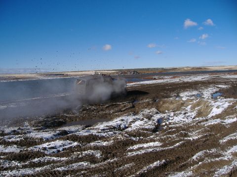 1979 Ford Bronco - An off-road vehicle navigates a challenging muddy and snowy terrain, creating a cloud of steam and spray.