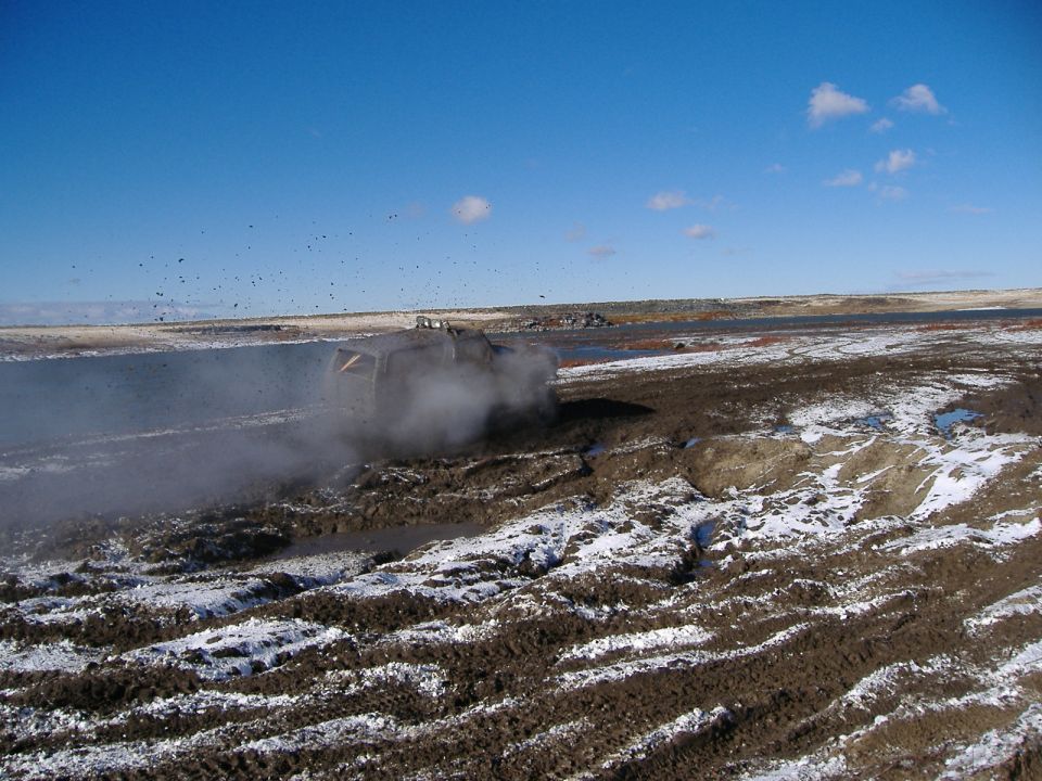 Off-road vehicle kicking up mud and steam in a snowy, muddy field