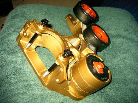 1992 Ford Probe - A gold-painted brake caliper with two small wheels is shown from an angled perspective on a green textured surface.