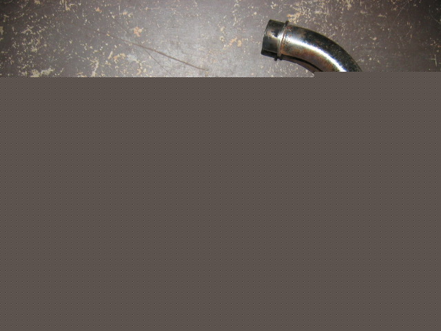 Curved chrome exhaust pipe with a black end cap, resting on a textured surface