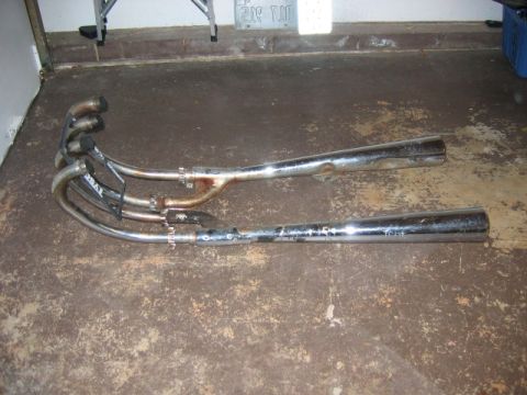 1985 Ford LTD Crown Victoria - Pair of chrome motorcycle exhaust pipes, showing some rust and wear, with visible branding on one pipe.