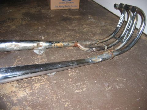 1985 Ford LTD Crown Victoria - A pair of used motorcycle exhaust pipes are shown on a textured surface, with some rust and wear visible.