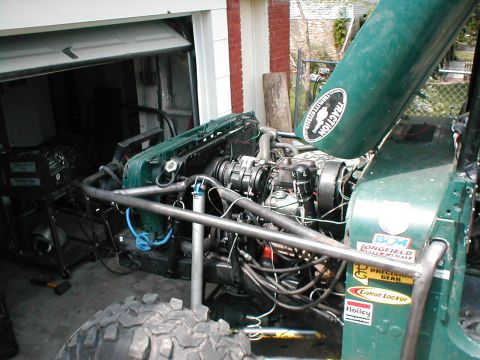 1983 Ford Bronco - The engine bay of a modified green off-road vehicle is shown, a custom roll cage and various aftermarket parts. The hood is open, revealing…