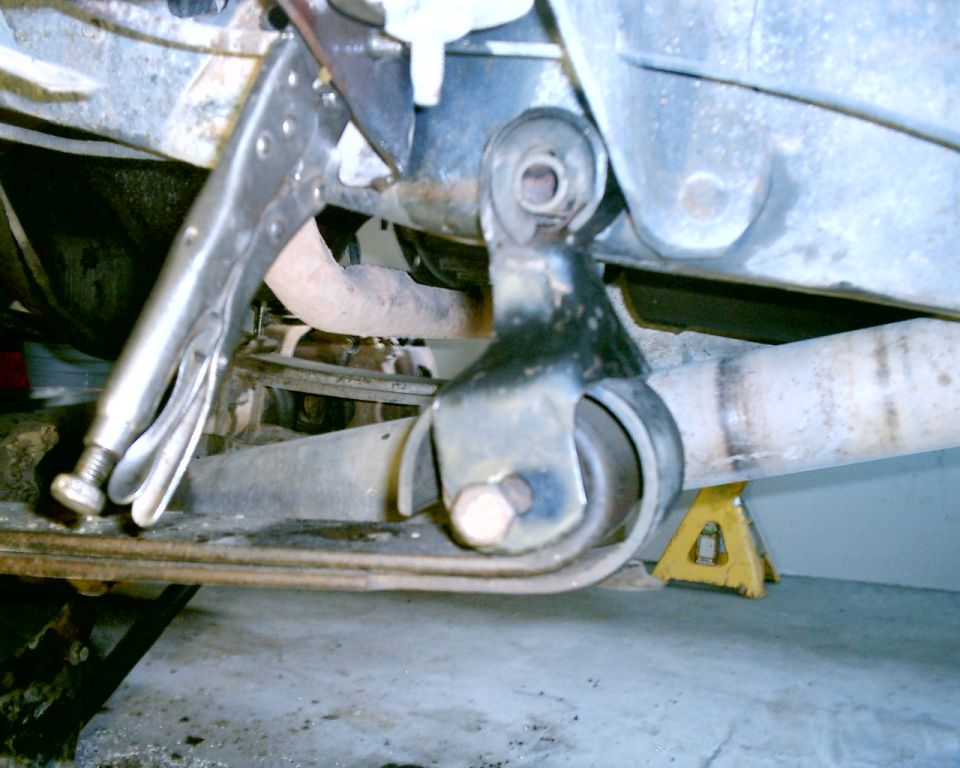 Vise grips clamped onto a vehicle's suspension component, with exhaust pipe visible and supported by a jack stand