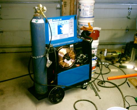 1985 Ford Bronco - A welding machine is set up in a garage, with a gas cylinder and spools of wire visible.