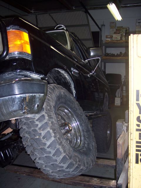 1988 Ford Bronco - A black SUV with oversized tires is positioned on a lift inside a garage or workshop.