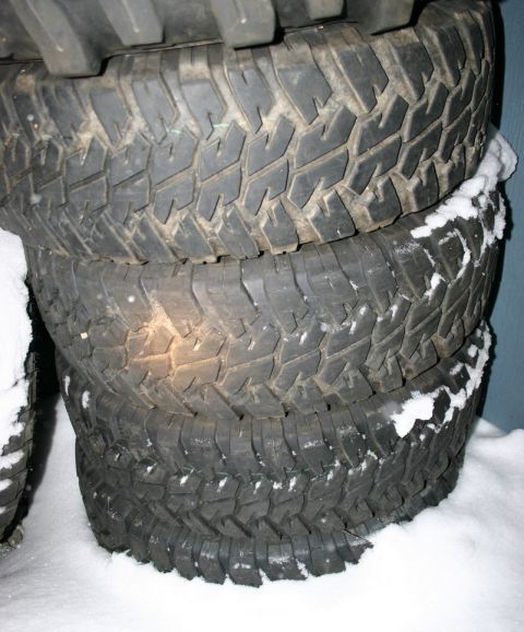 2003 Jeep TJ - Four off-road tires are stacked on top of each other, covered in a light dusting of snow.