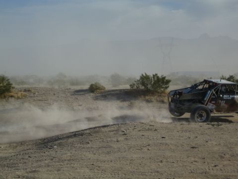 Black off-road race buggy speeding away in a thick desert dust cloud