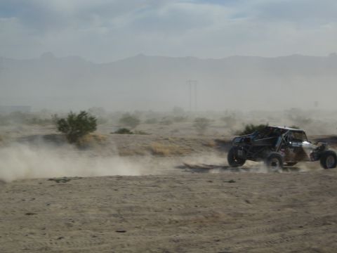Off-road race buggy speeding across desert with a heavy dust trail and mountains