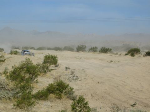 Off-road buggy at left on a sandy desert ridge with hazy mountains behind