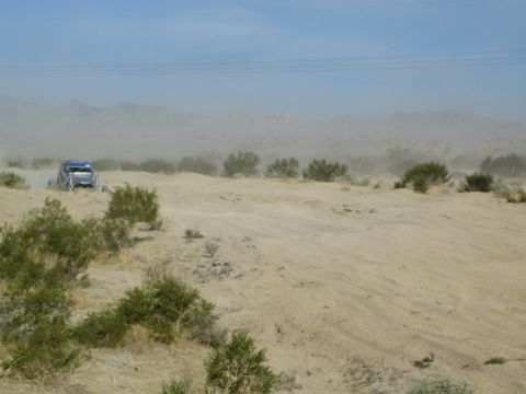Blue off-road buggy at left on a sandy desert ridge with mountains behind