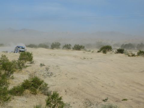 Blue off-road buggy at left on a brushy sandy desert ridge under hazy sky