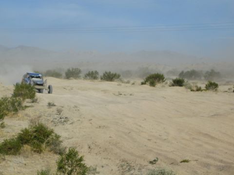 Blue off-road race buggy kicking up dust on a desert sand wash under a hazy sky