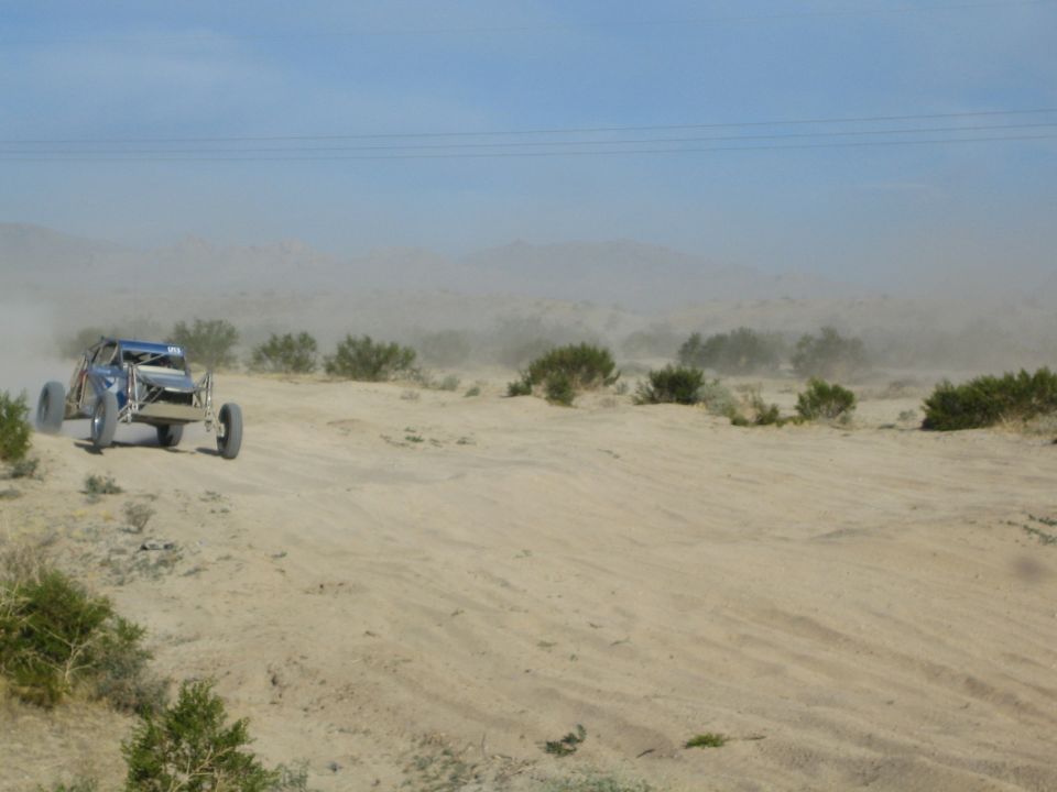 Side view of a blue tube-frame sand buggy on desert dunes with dust haze behind