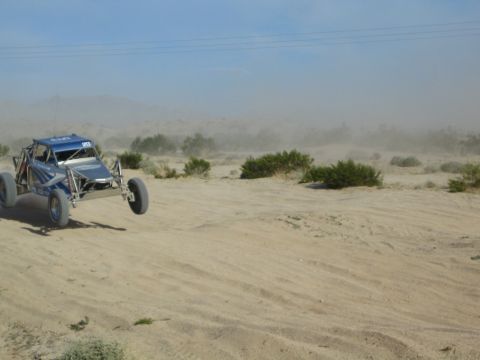 Blue tube-frame race buggy driving across desert sand throwing up dust
