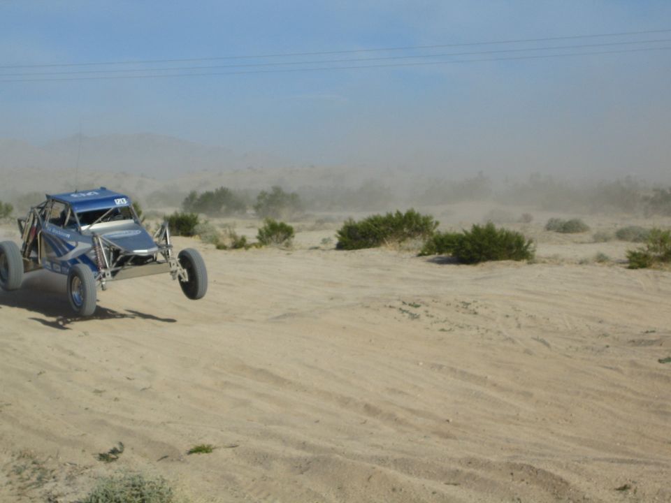 Blue tube-frame race buggy driving across desert sand throwing up dust