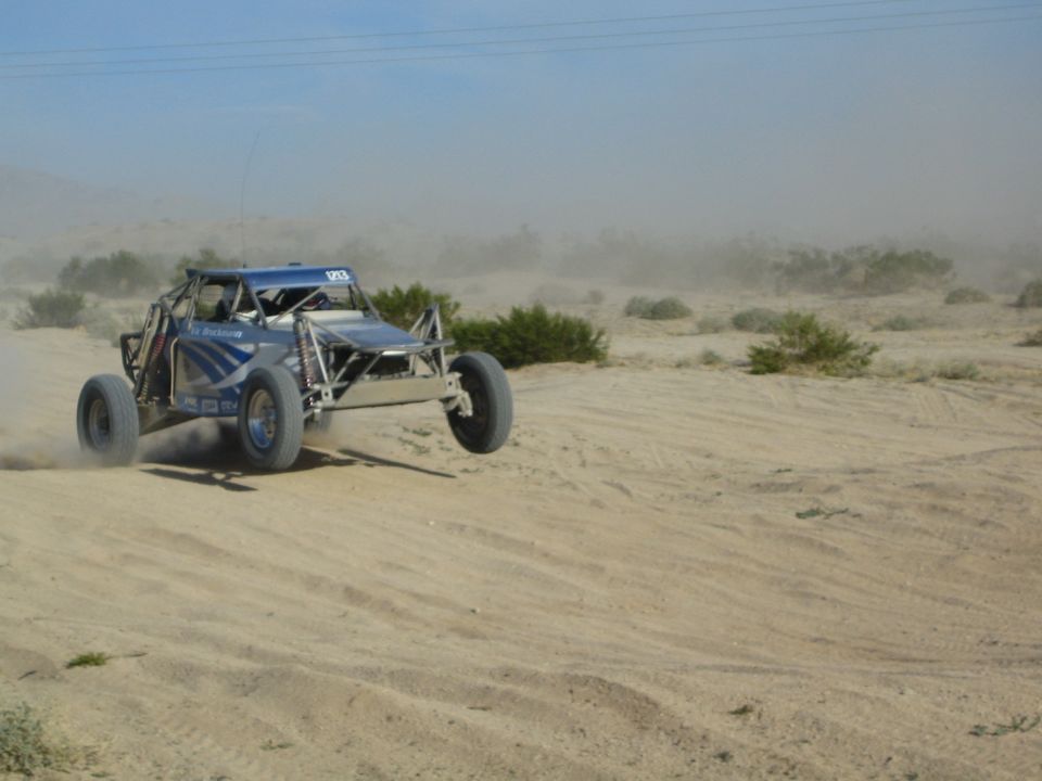Blue off-road race buggy at speed throwing sand and dust in the desert