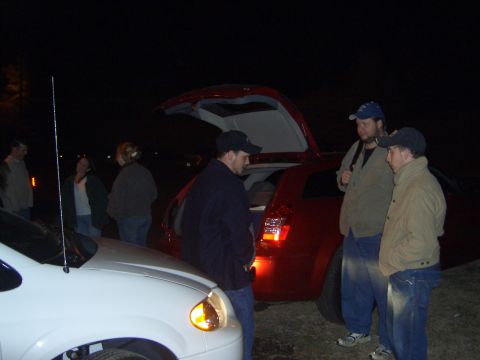 1996 Ford Bronco - Several people stand around a red SUV at night with its rear hatch open, while a white car is parked nearby.