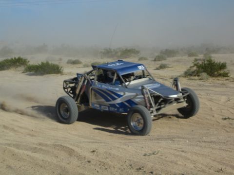 Blue and silver off-road race buggy sliding through desert sand in a cloud of dust