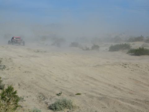 Distant red off-road buggy on a sandy desert ridge nearly hidden by dust haze
